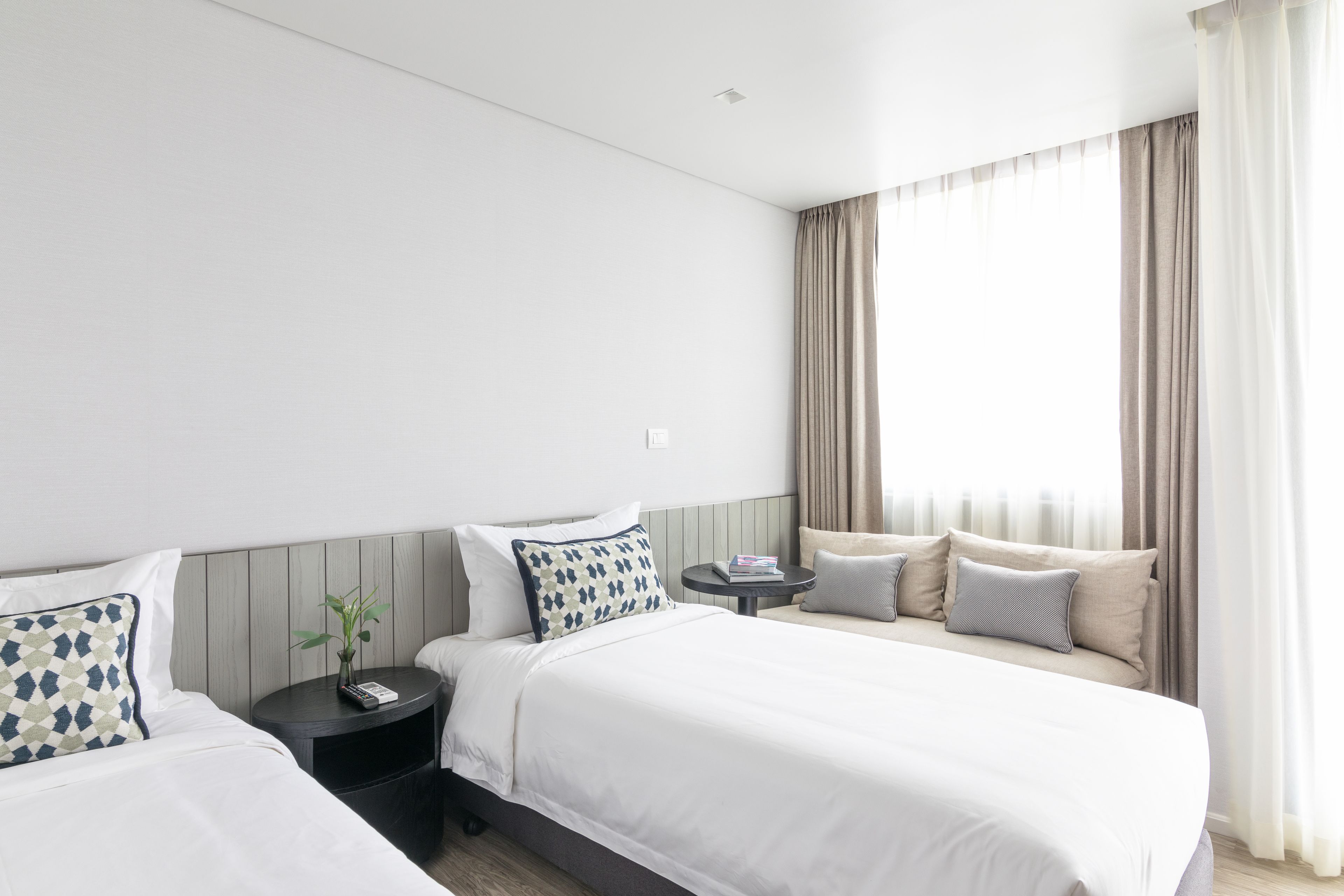 Hotellihuone, jossa on kaksi sänkyä, pieni pöytä ja yöpöytä.
