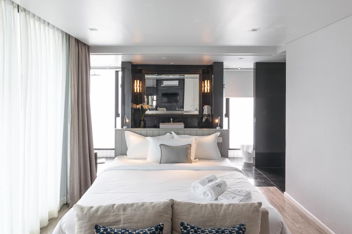 Une chambre d’hôtel moderne avec un grand lit, une table de chevet sur laquelle se trouvent un livre et un vase, et une vue sur la salle de bain.