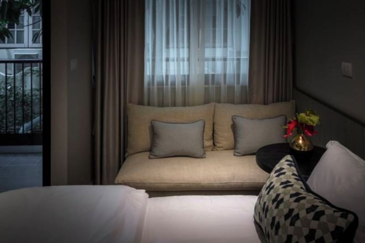 Une chambre d’hôtel avec un lit, un canapé et une petite table sur laquelle est posé un vase de fleurs.