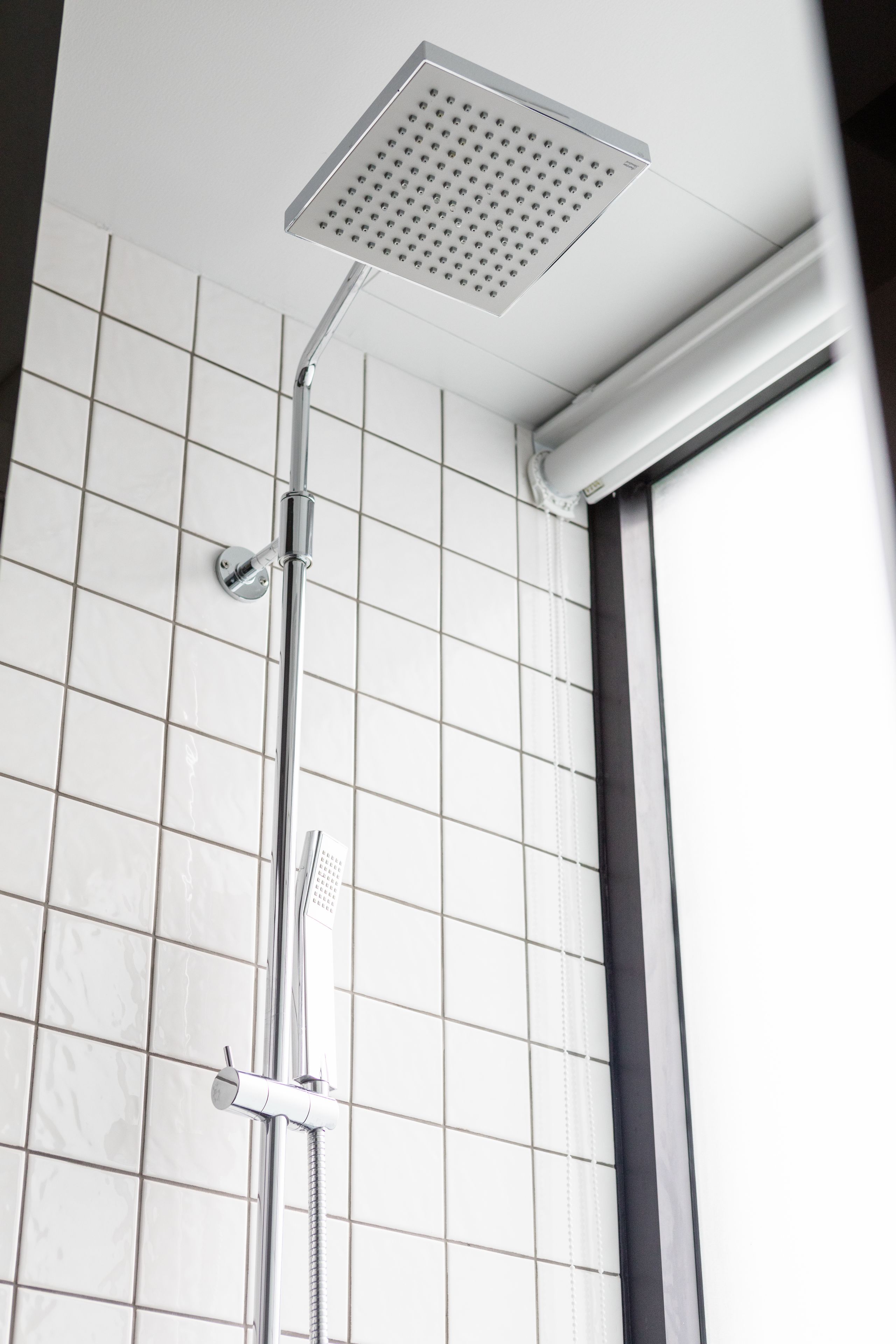 A modern shower with a square head, a handheld showerhead, and a wall-mounted control valve.