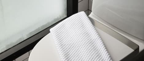 A white toilet with a white towel on the seat, a visible flush handle, and a tiled wall with a black border.