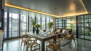 Un comedor moderno con una mesa y sillas de madera, un sofá y ventanas amplias que ofrecen vista a la ciudad.