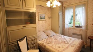 Une chambre à coucher avec un lit, une chaise, une commode et une fenêtre avec des rideaux.