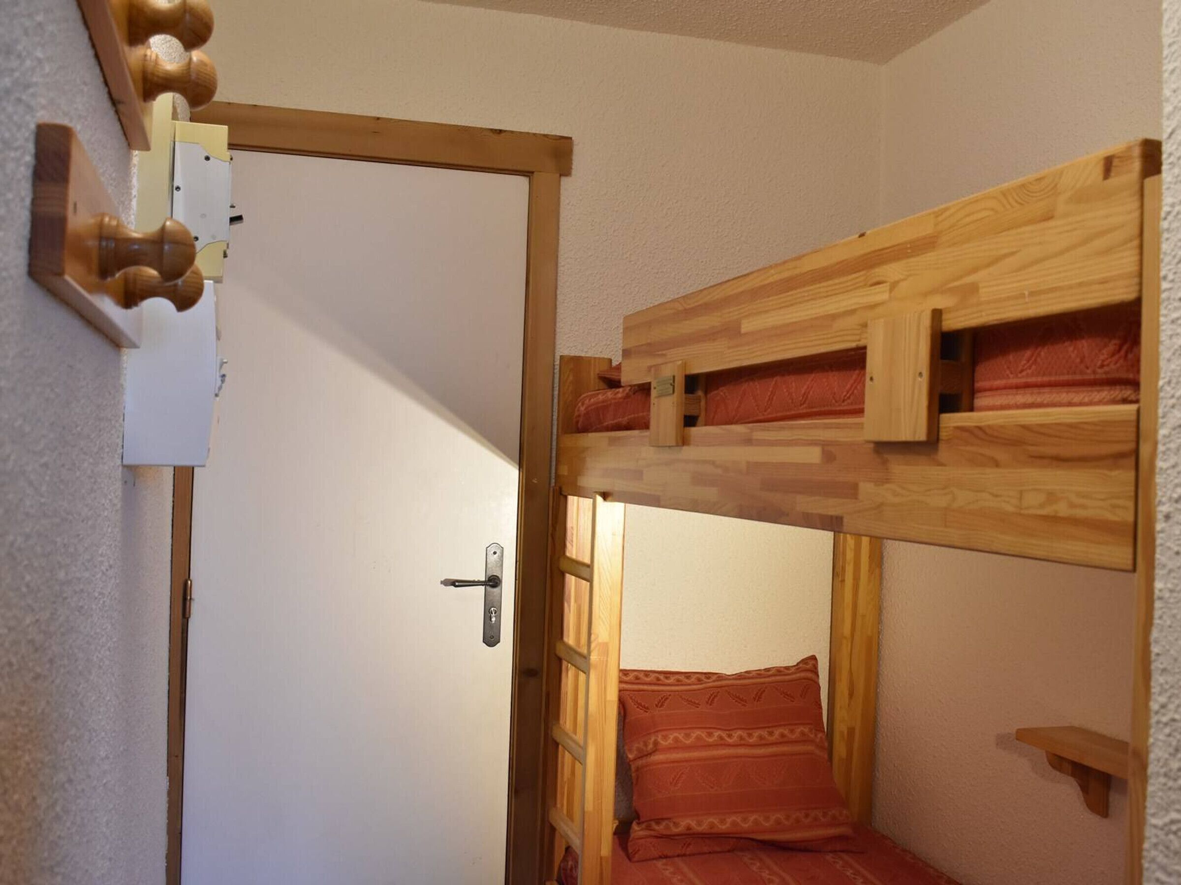 A room with a wooden bunk bed, a door with a handle, and a small shelf.