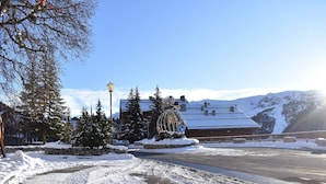 A snow-covered landscape with a building featuring a traditional chalet style, surrounded by snow-laden trees and a clear sky. - Cozy Studio for 4 Near Slopes and Shops in Méribel (Méribel)