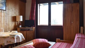 A wooden room with a bed, a table with a lamp, a television, and a window with curtains. - Cozy Studio for 4 Near Slopes and Shops in Méribel (Méribel)