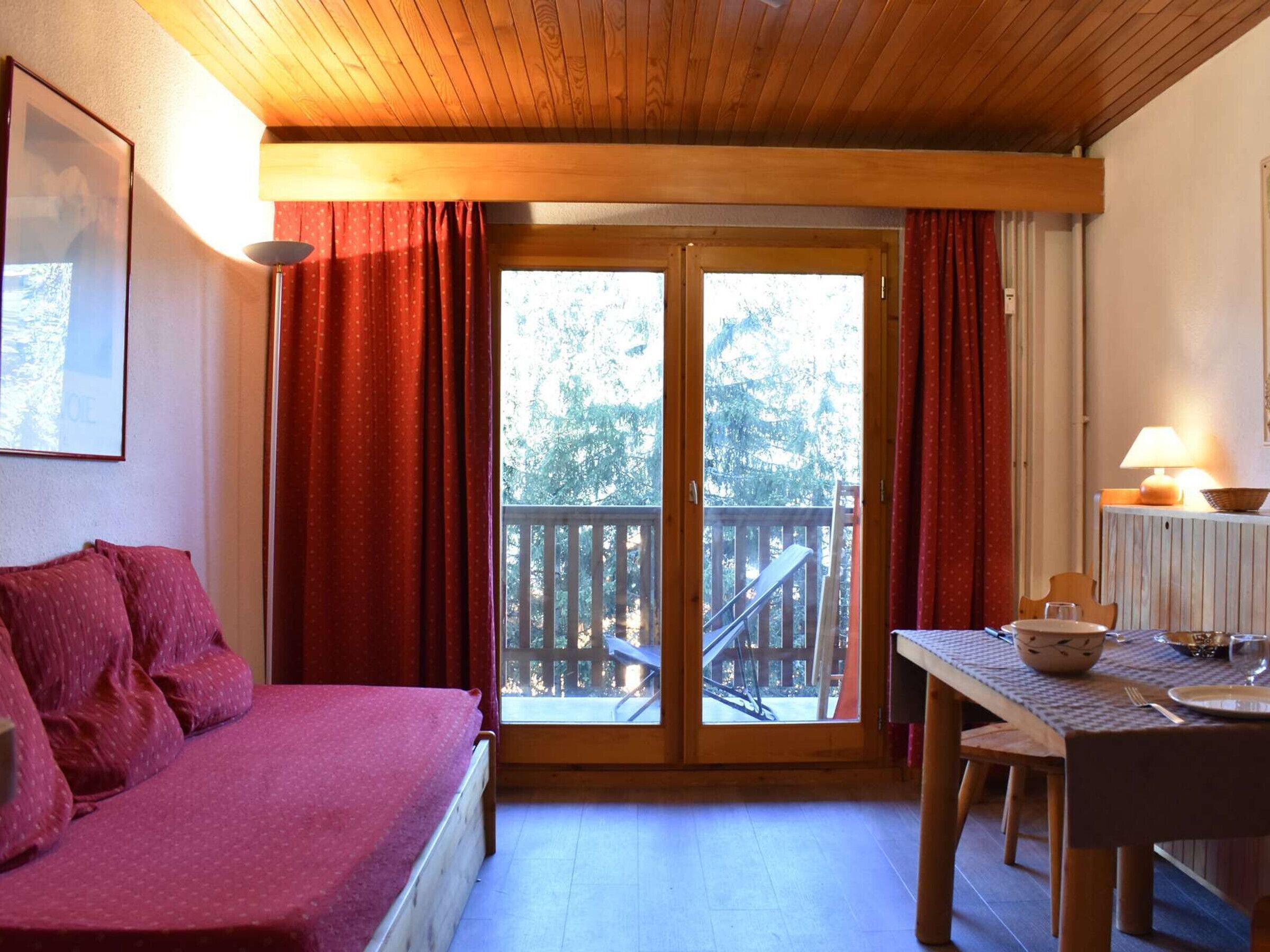 A room with a bed, a table with a bowl and a glass, and a balcony with a wooden railing.
