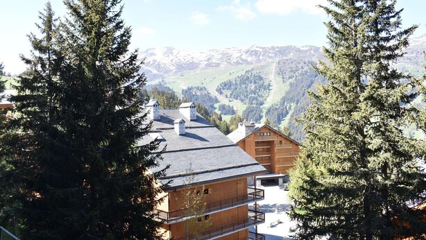 Eine Holzhütte mit mehreren Balkonen, umgeben von hohen Kiefern und einer Berglandschaft im Hintergrund.