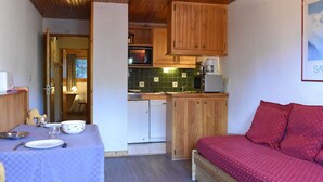 Eine kleine Küche mit Holzausstattung, einem Esstisch mit kariertem Tischläufer und einem Bett mit roter Bettwäsche.
