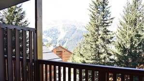 Ein Balkon mit Blick auf eine Berglandschaft, ein Holzhaus und hohe Nadelbäume.
