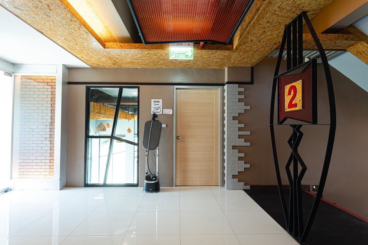 A modern interior with a tiled floor, a door with a sign, a wall-mounted number, and a ceiling with a wooden beam.