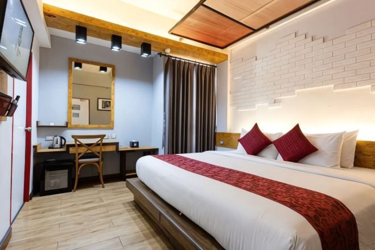 A hotel room with a bed, desk, chair, and a mirror.