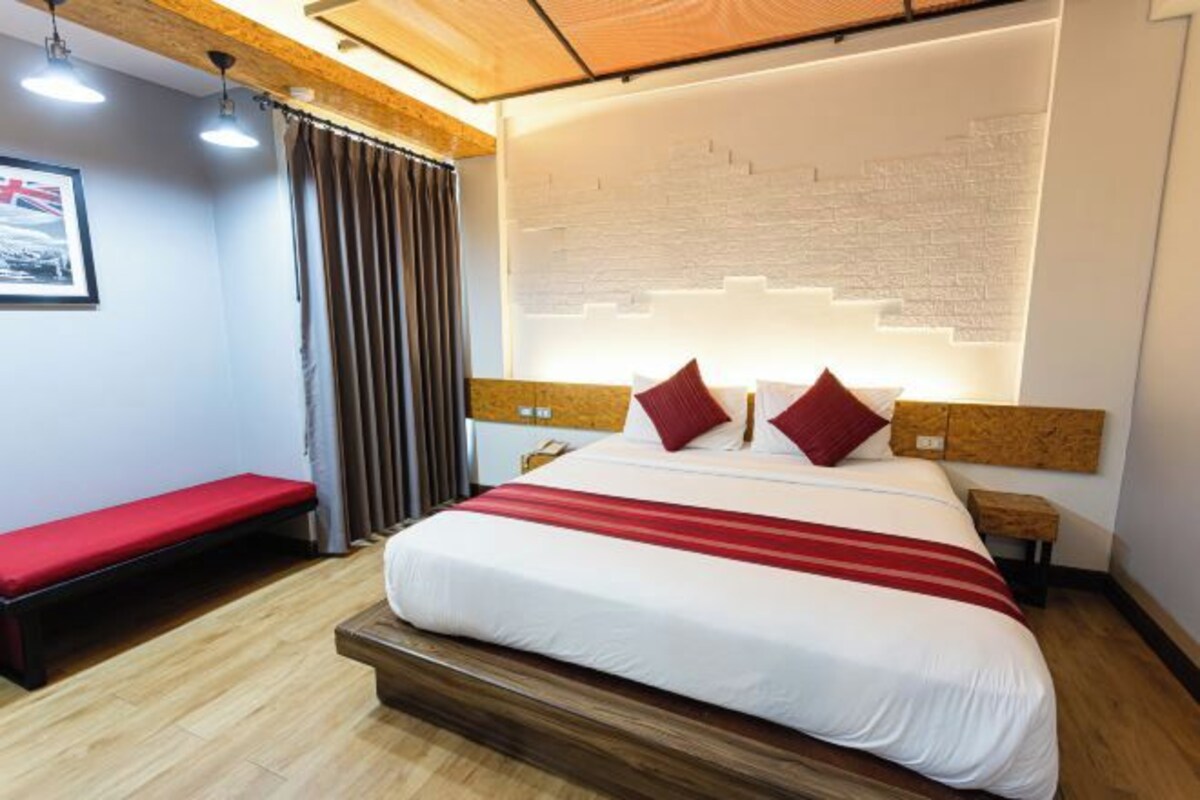 A hotel room with a bed, a bench, a nightstand, and a wall with a brick pattern.