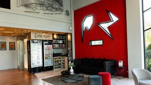 A hotel lobby with a red wall, a black sofa, a grey armchair, a coffee table, and a refrigerator. - PS Sriphu Hotel (Hat Yai)
