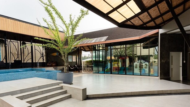 A modern outdoor pool area with a glass enclosure, steps leading to the pool, and a large potted plant. - PS Sriphu Hotel (Hat Yai)