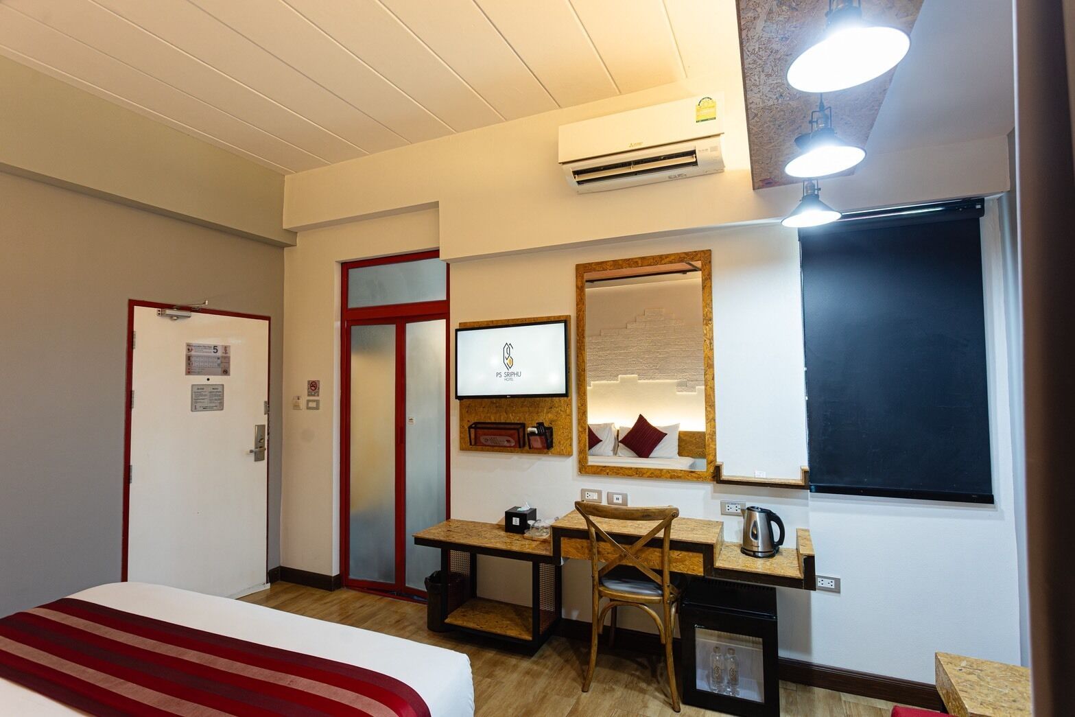 A hotel room with a bed, desk, chair, TV, and an air conditioning unit.