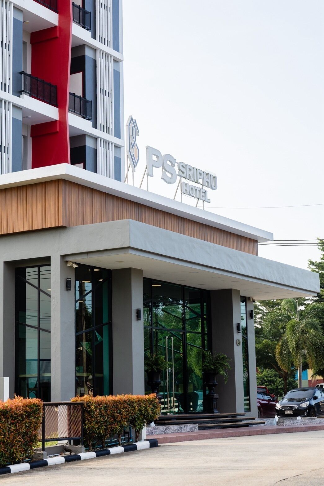 A modern hotel with a prominent PS sign, large glass windows, and a red accent on the facade.