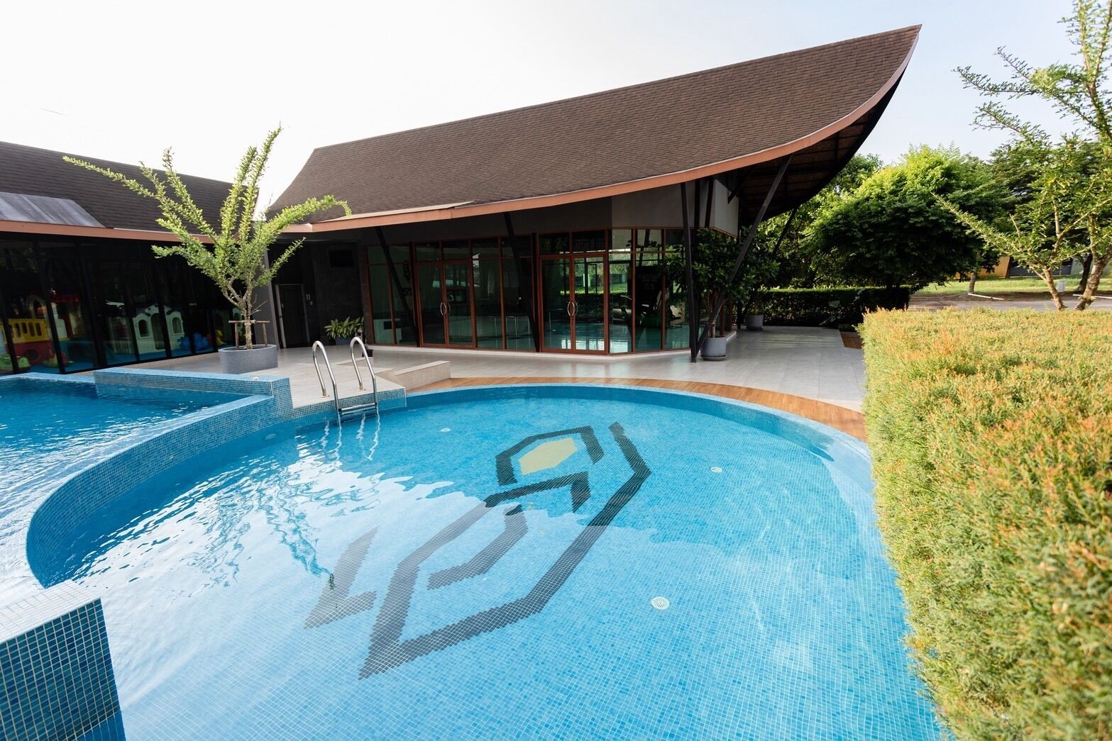 Un edificio moderno con piscina, puertas de vidrio y techo curvo.