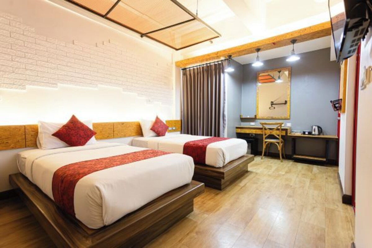 A hotel room with two beds, a desk, a chair, a mirror, and a window with curtains.