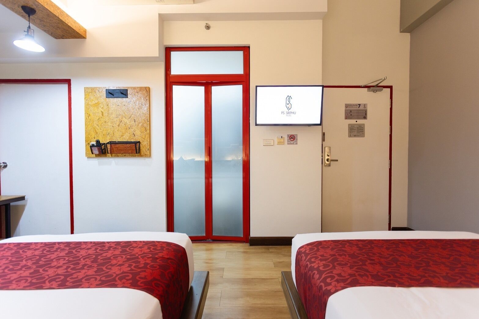 Een hotelkamer met twee bedden, een televisie, een houten plafond en een rode deur.