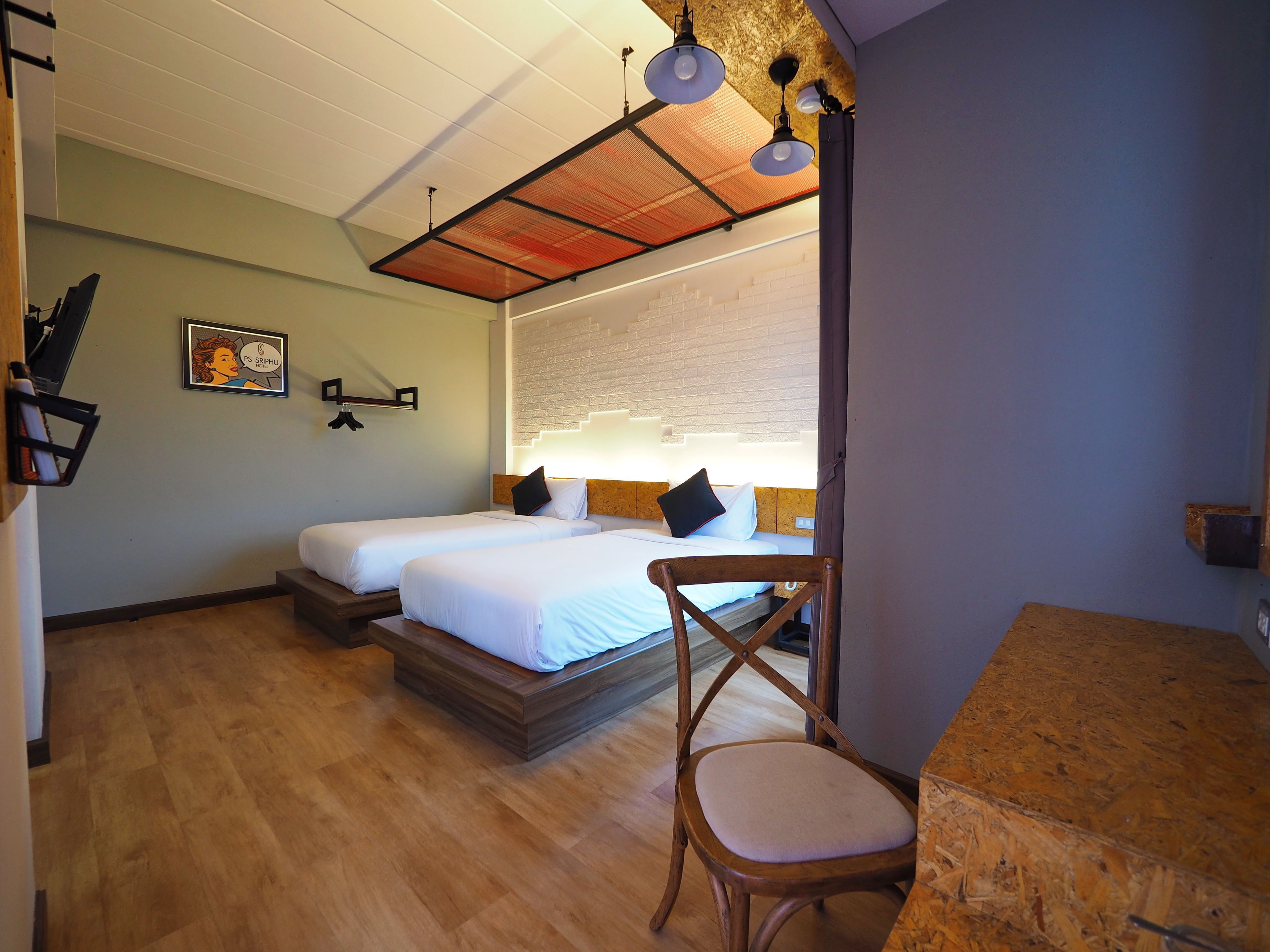 A hotel room with two beds, a wooden desk, a chair, a ceiling fan, and a wall-mounted light fixture.