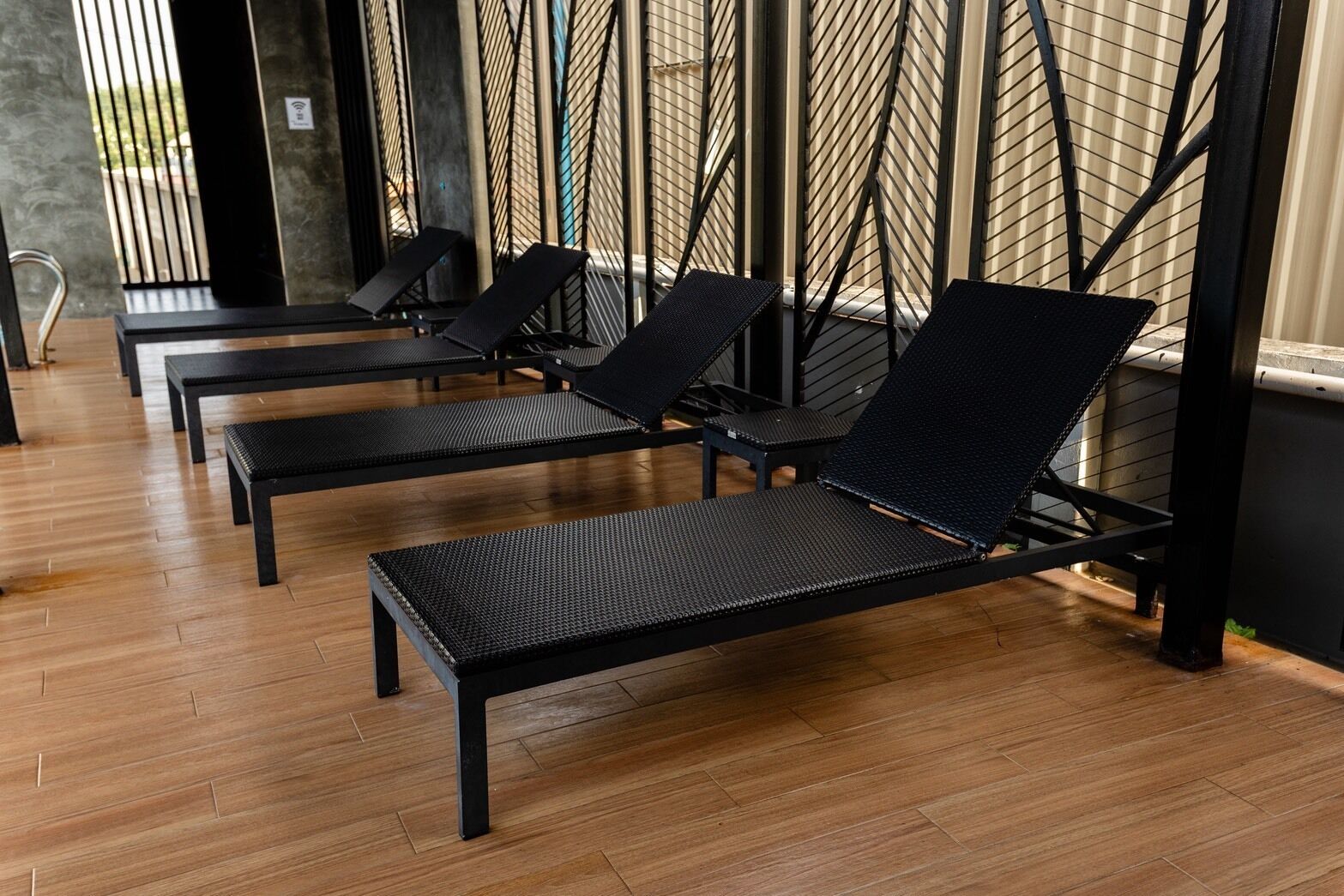 Une rangée de fauteuils noirs, dotés d’assises et de dossiers en osier tressé, est disposée sur un plancher en bois dans une pièce dont un mur est orné d’un motif métallique.