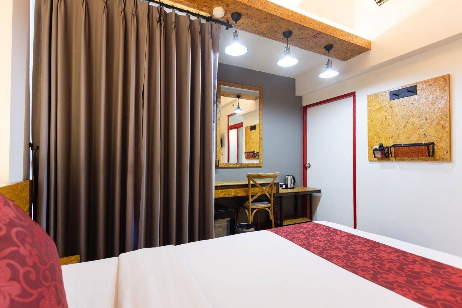 A hotel room with a bed, a desk, a chair, a mirror, and a red accent wall.