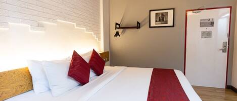 A hotel room with a bed, a red and white bedspread, a red and white pillow, a picture on the wall, and a door with a sign.