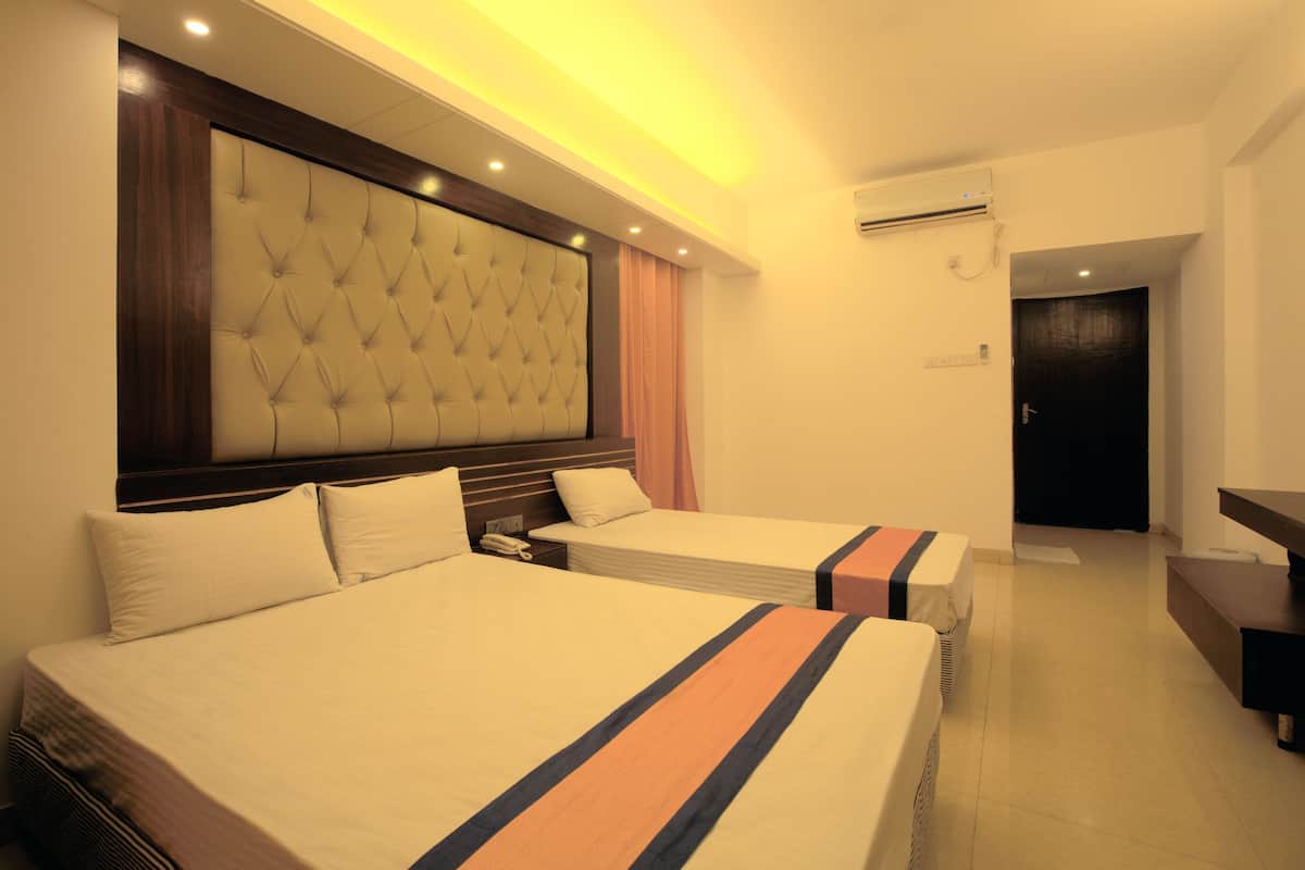 A hotel room with two beds, a large tufted headboard, a bedside table with a phone, and an air conditioning unit on the wall.