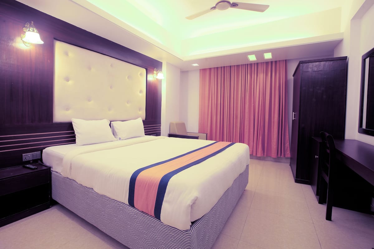 A hotel room with a large bed, a desk, a wardrobe, and a ceiling fan.