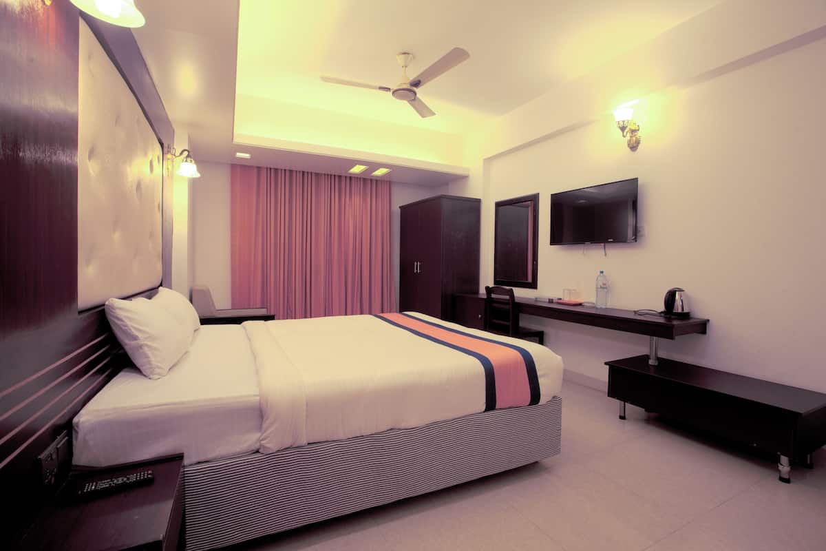 A modern hotel room with a bed, bedside table, desk, chair, TV, ceiling fan, and a large window with curtains.