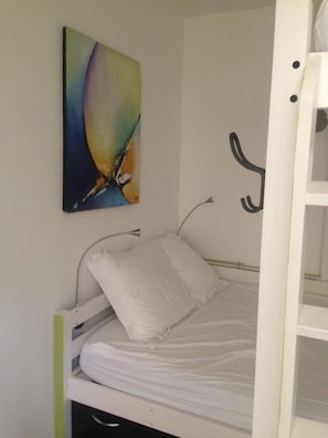 Una cama individual con ropa de cama blanca en una habitación con pared blanca.