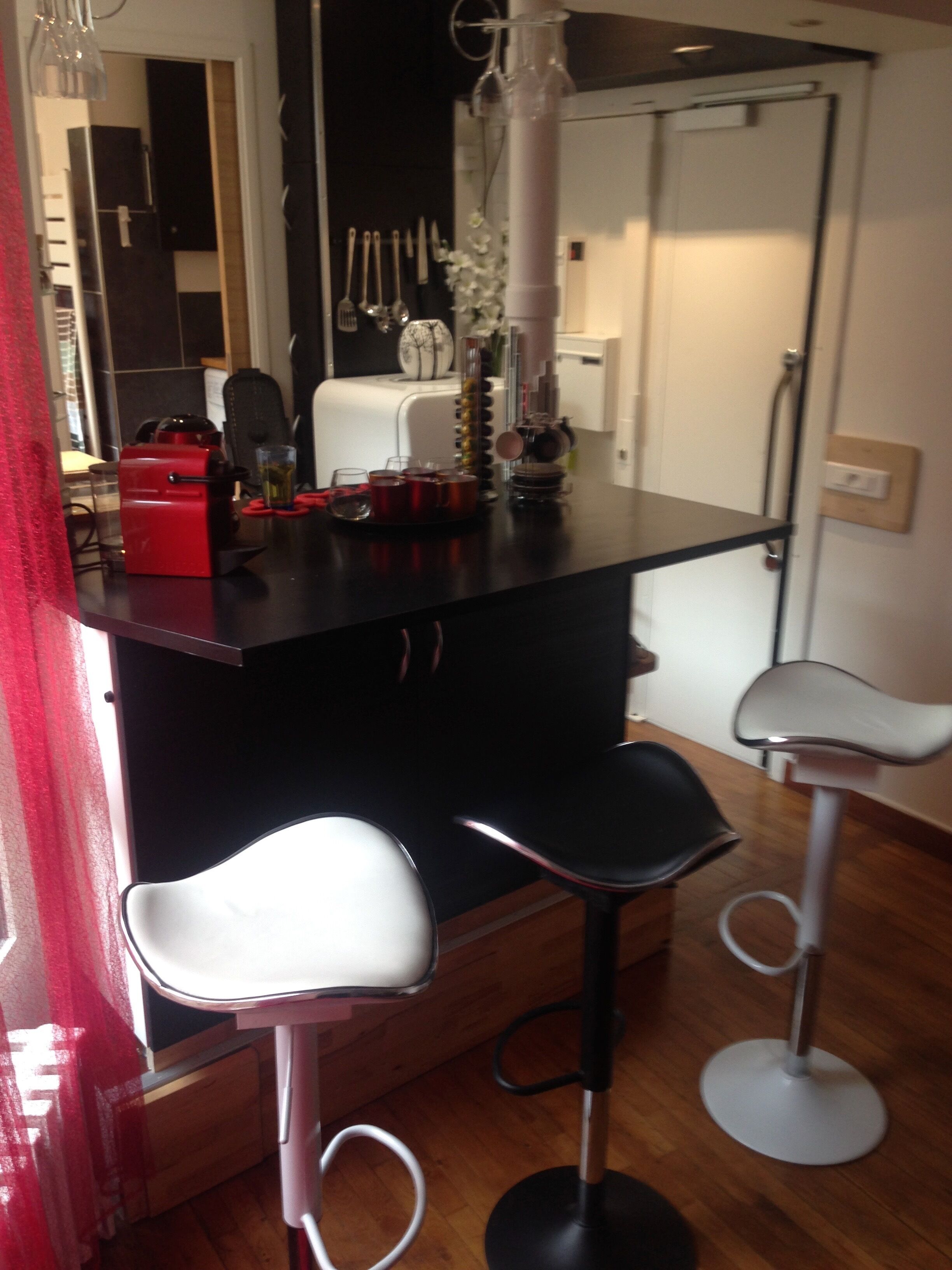 A kitchen with a black countertop, three white bar stools, a red appliance, and various kitchen utensils.