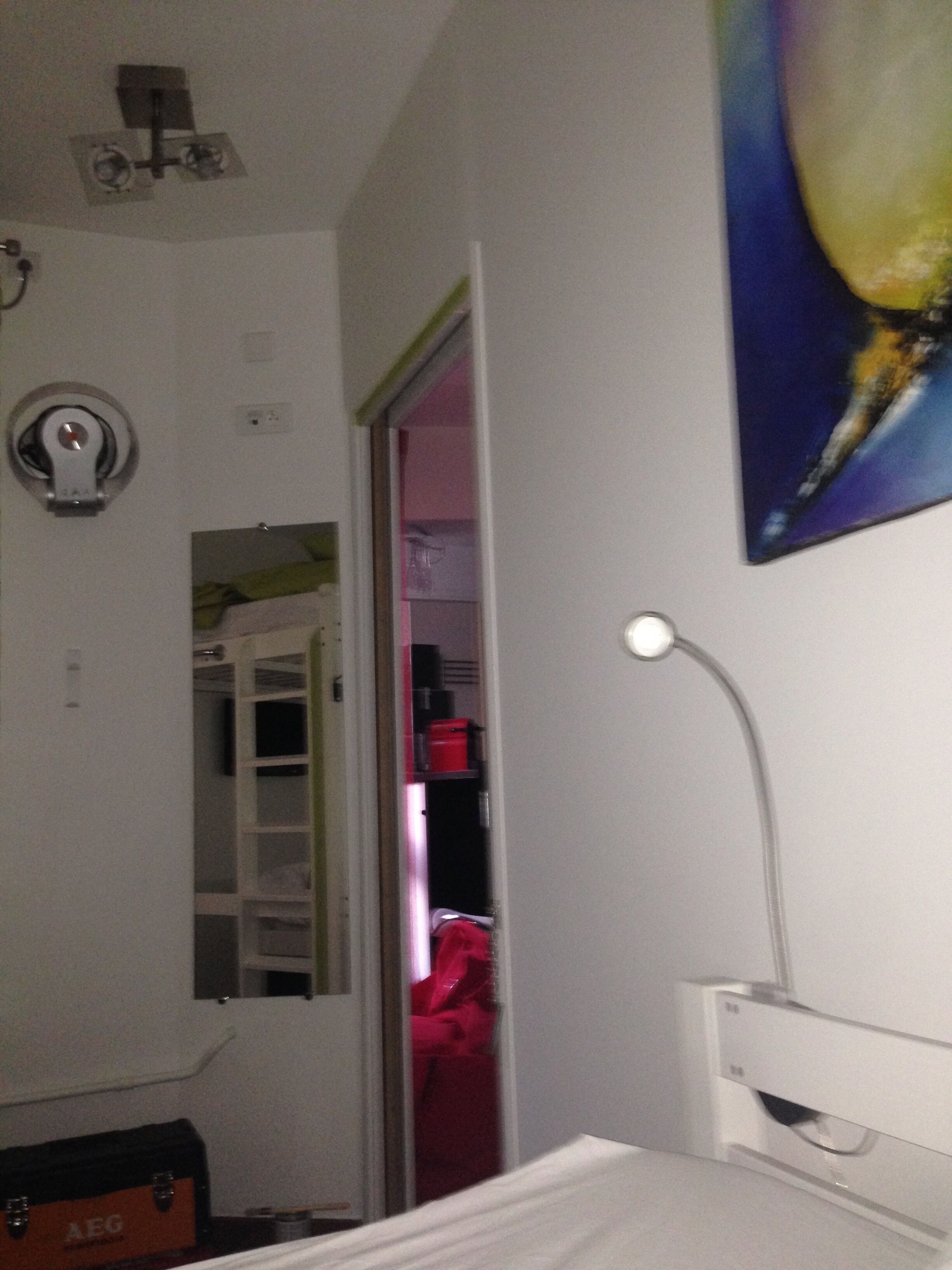A bedroom with a bed, a bedside table, a lamp, a wardrobe, and a mirror.