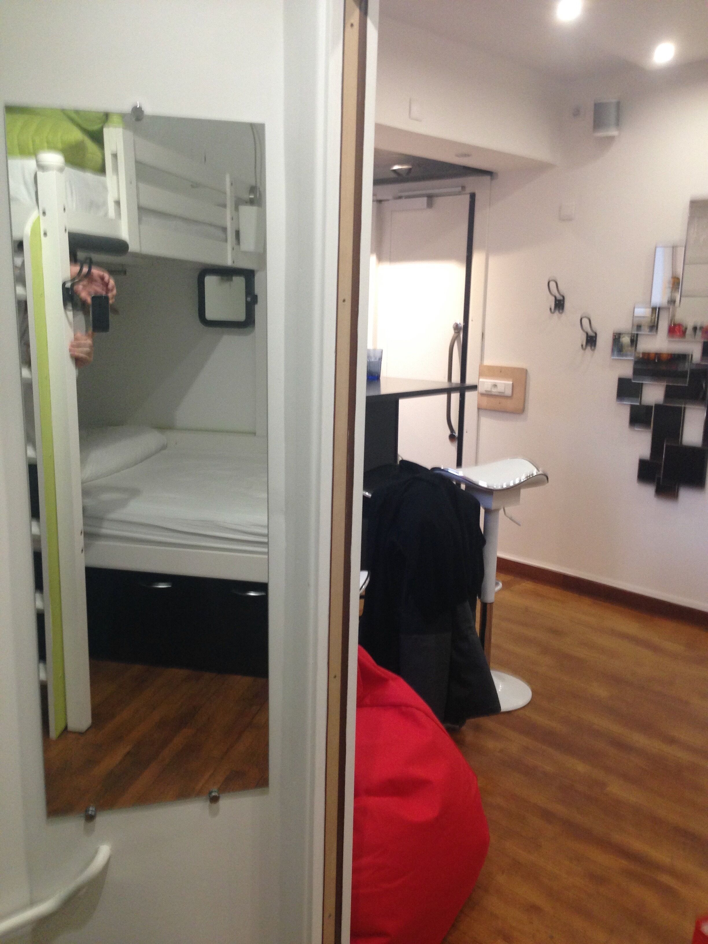 Una habitación con una cama litera, un escritorio con silla, un espejo y un sillón de peluche rojo.