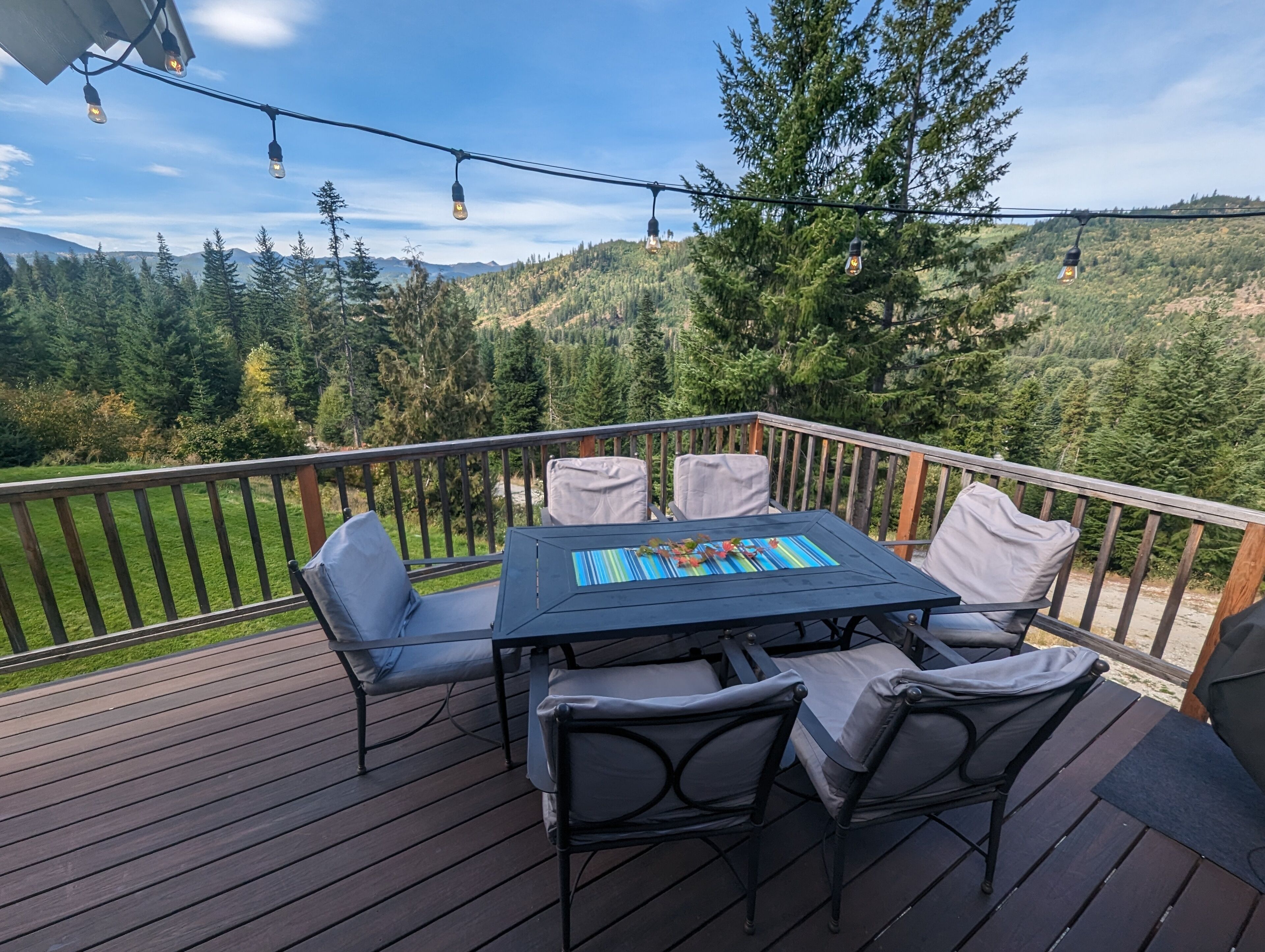 Um terraço com mesa e cadeiras, com vista para uma paisagem arborizada.