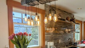 Una cocina moderna con salpicadero de piedra, una isla grande con un jarrón de flores e iluminación colgante.