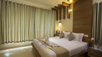 A hotel room with a large bed, a wooden headboard, a nightstand with a vase of flowers, and a window with curtains.