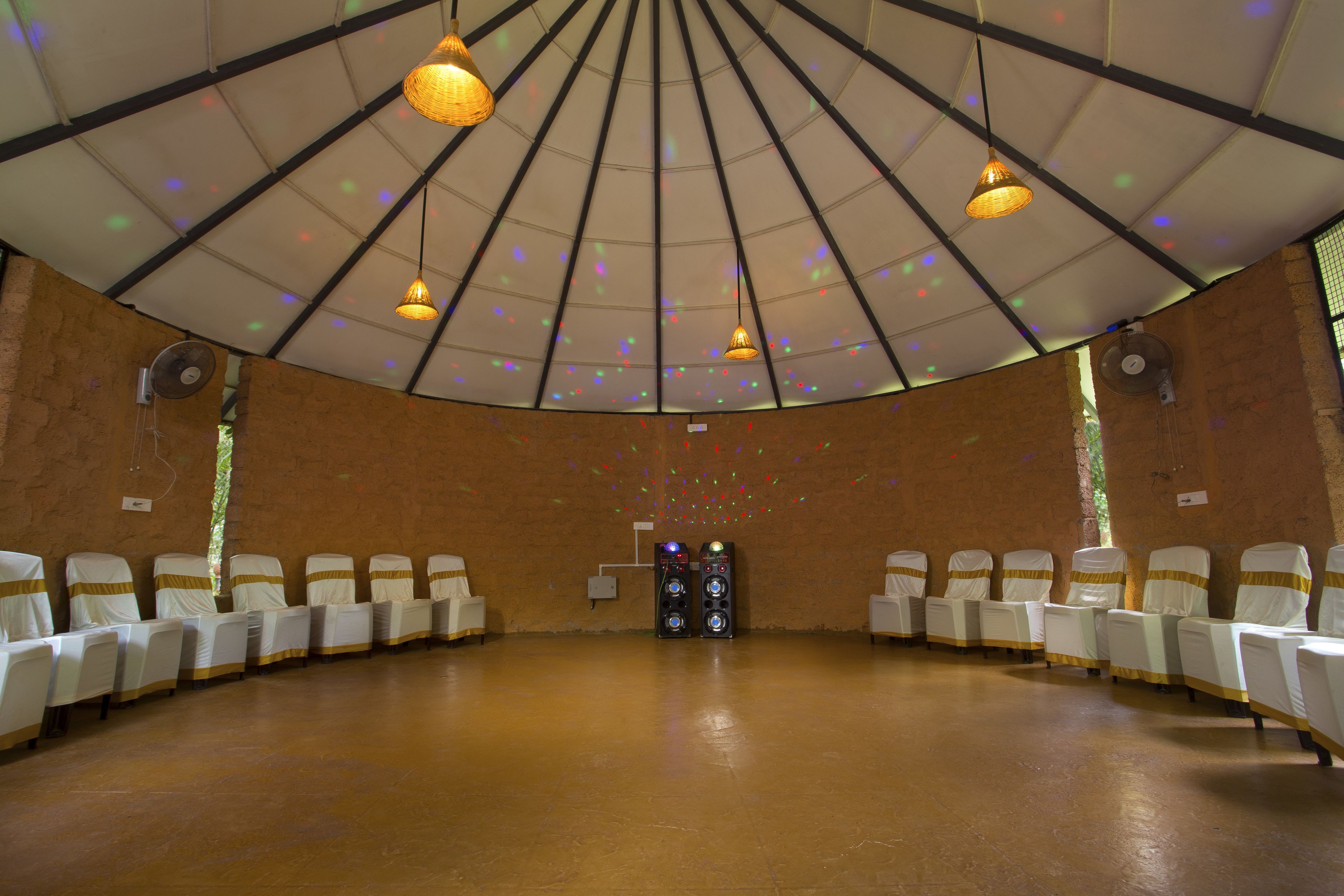Une salle circulaire avec des chaises et des tables blanches, un plafond orné de luminaires suspendus et une boule à facettes.