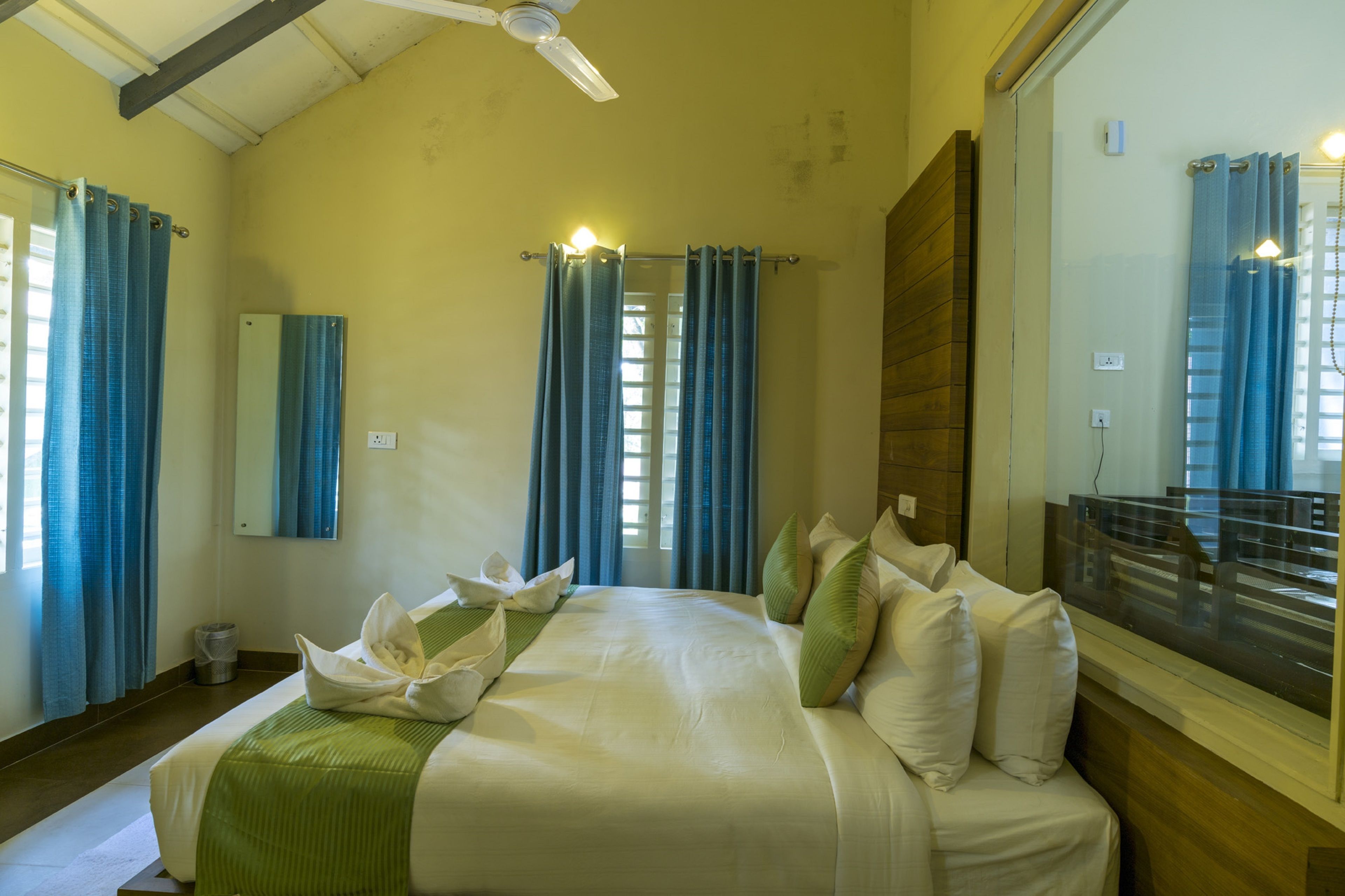 Quarto de hotel com uma cama grande, ventoinha no teto, janela com cortinas e vista para o exterior.