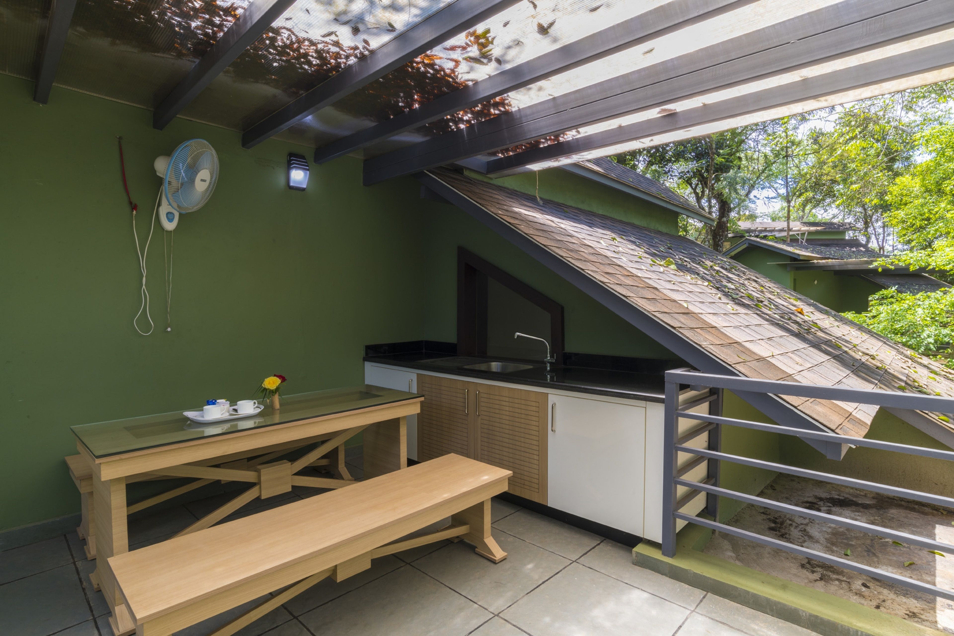 A small kitchen with a sink, a fan, and a table with a bench.