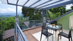 Un balcon avec une table en verre, des chaises et une vue sur un paysage montagneux.