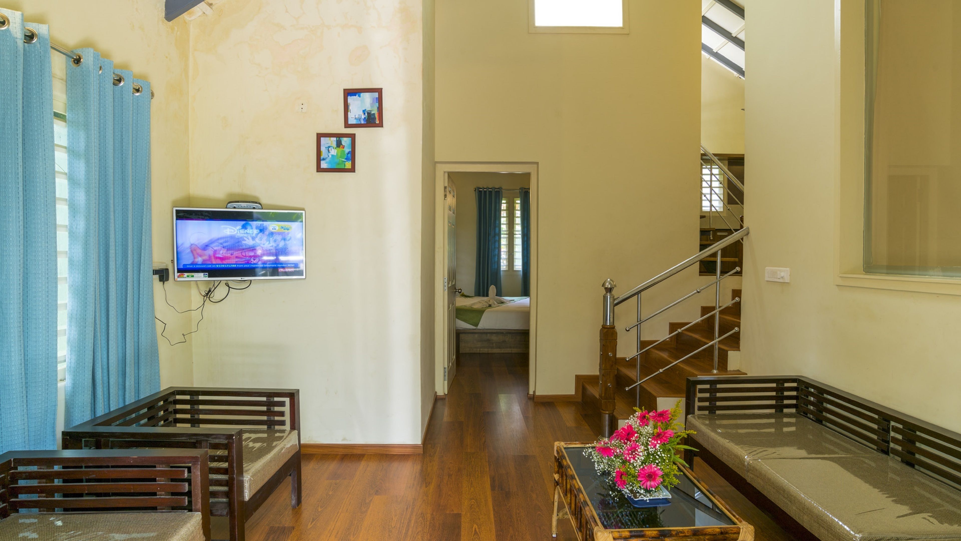 A living room with a TV mounted on the wall, a wooden bench, a sofa, and a staircase leading to another room.