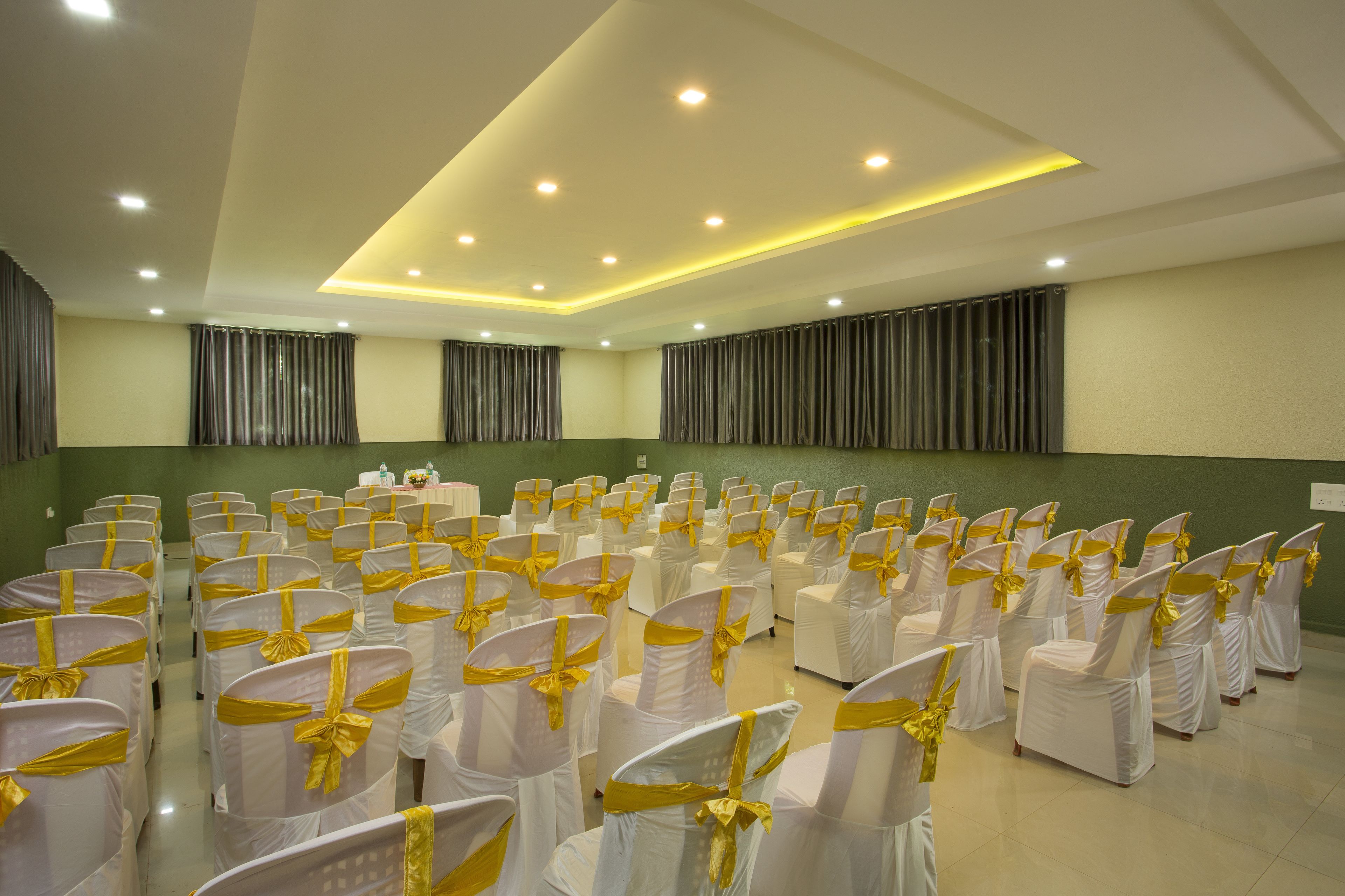 A conference room with rows of white chairs with yellow sashes, a podium, and green walls.