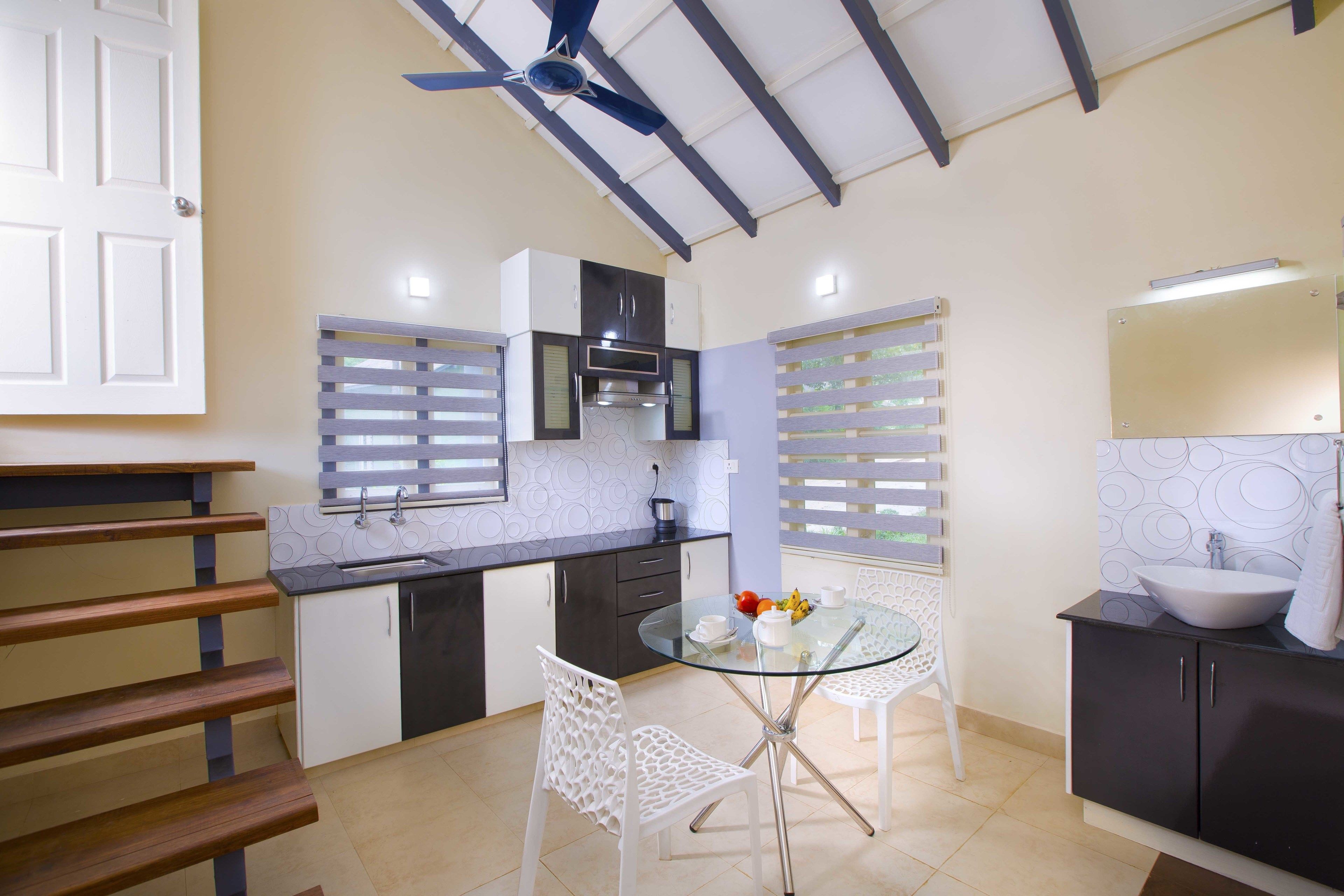 A modern kitchen with a glass dining table, white chairs, and a black countertop.