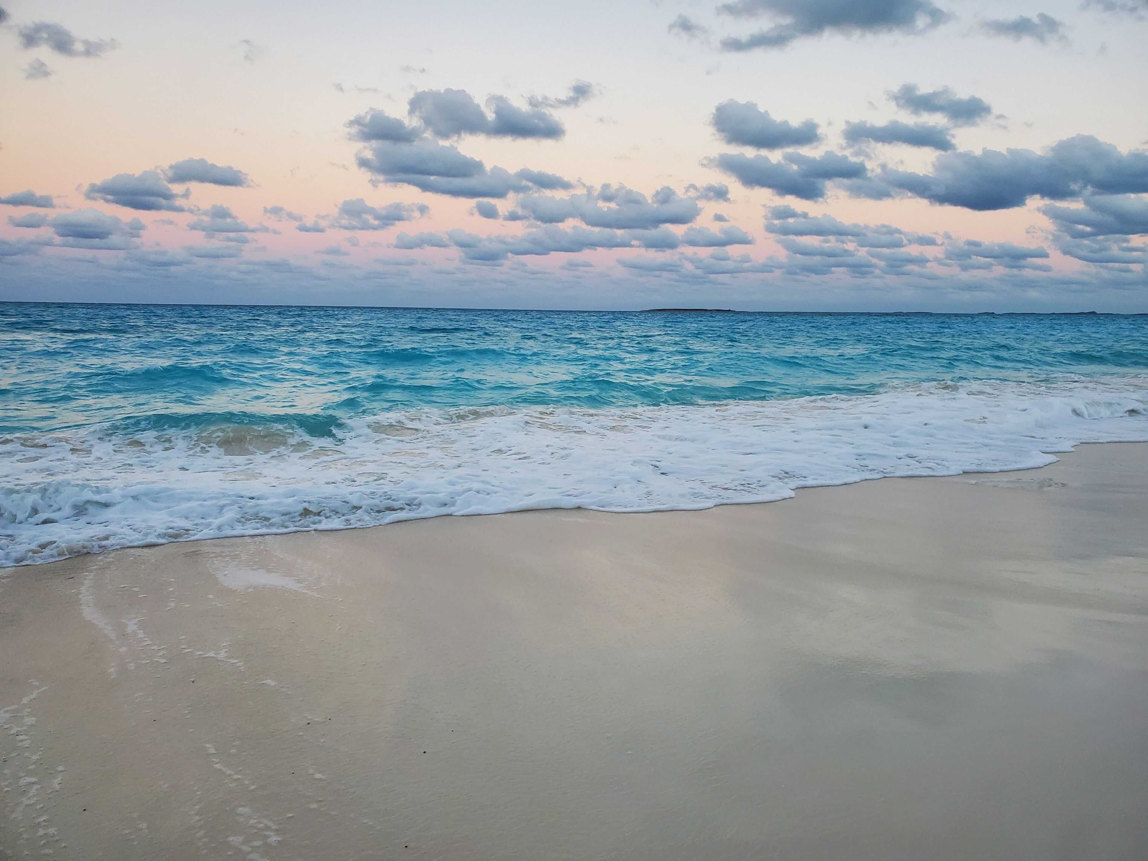 Ein Strand mit sanft anschwellenden Wellen, unter einem teils bewölkten Himmel.