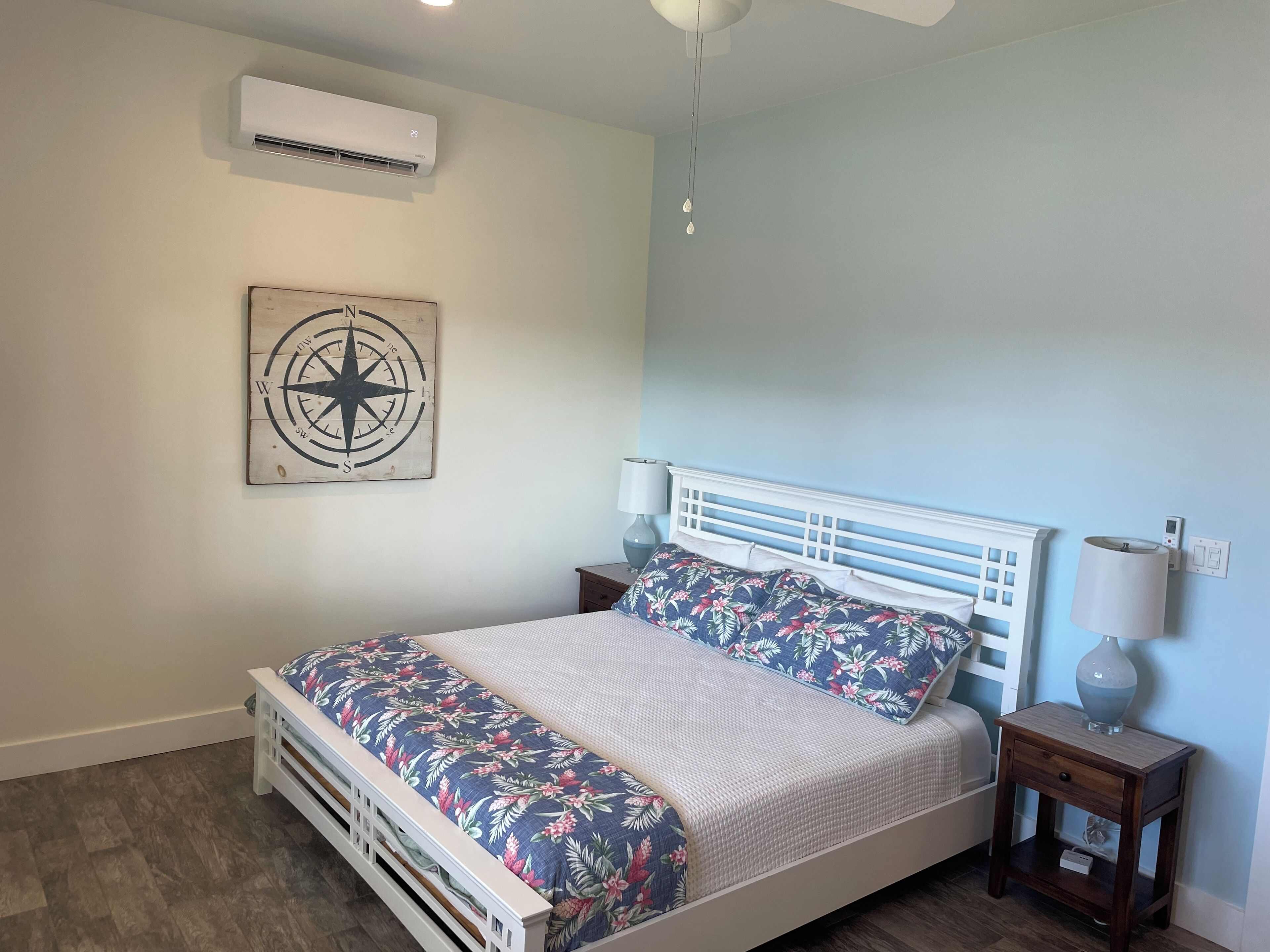 Een slaapkamer met een bed, nachtkastje, lamp, airconditioning en een aan de muur bevestigd kompas.