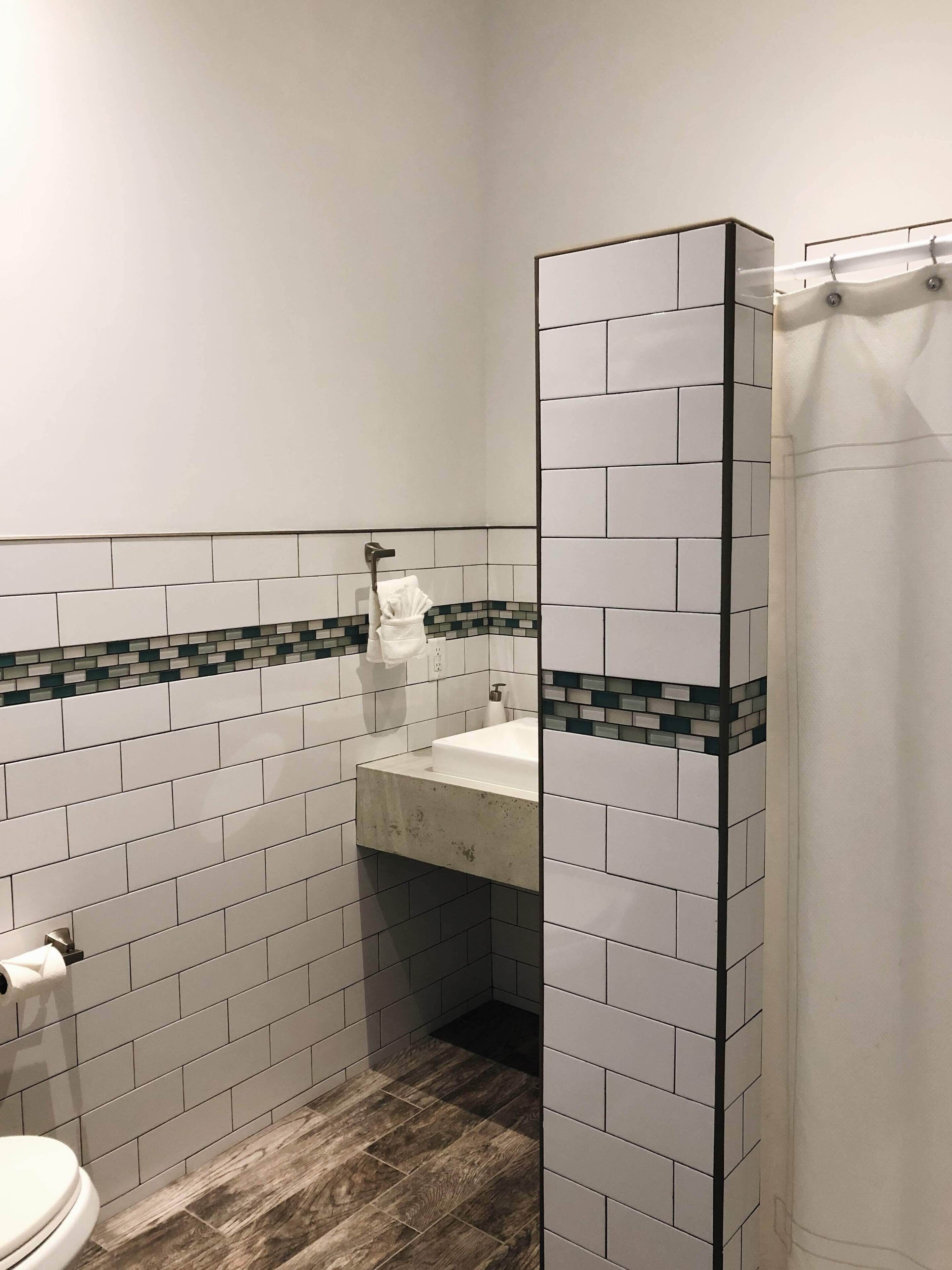 Ein Badezimmer mit weißen Fliesen im U-Bahn-Stil, Holzboden, Waschbecken in Weiß und Toilette.
