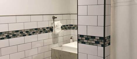 Ein Badezimmer mit weißen Fliesen im U-Bahn-Stil, Holzboden, Waschbecken in Weiß und Toilette.