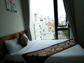 A hotel room with a large bed, a view of buildings through the window, and a curtain. - Bao Chau Hotel (Da Nang)